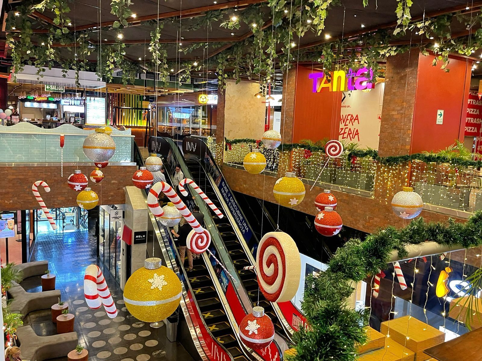 An indoor shopping mall with escalators, Christmas decorations, and a pizza restaurant.
