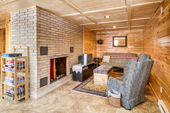 A cozy living room with a brick fireplace, wooden walls, a TV, and a patterned rug.