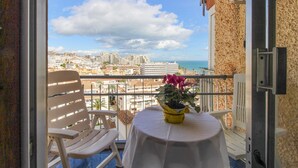 Un balcón con una mesa y sillas, una planta en maceta y vistas de una ciudad costera.