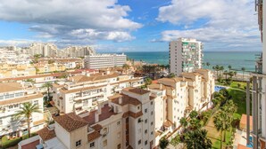 Un paisaje urbano costero con edificios residenciales, un hotel destacado con piscina en la azotea y una vista despejada del mar.