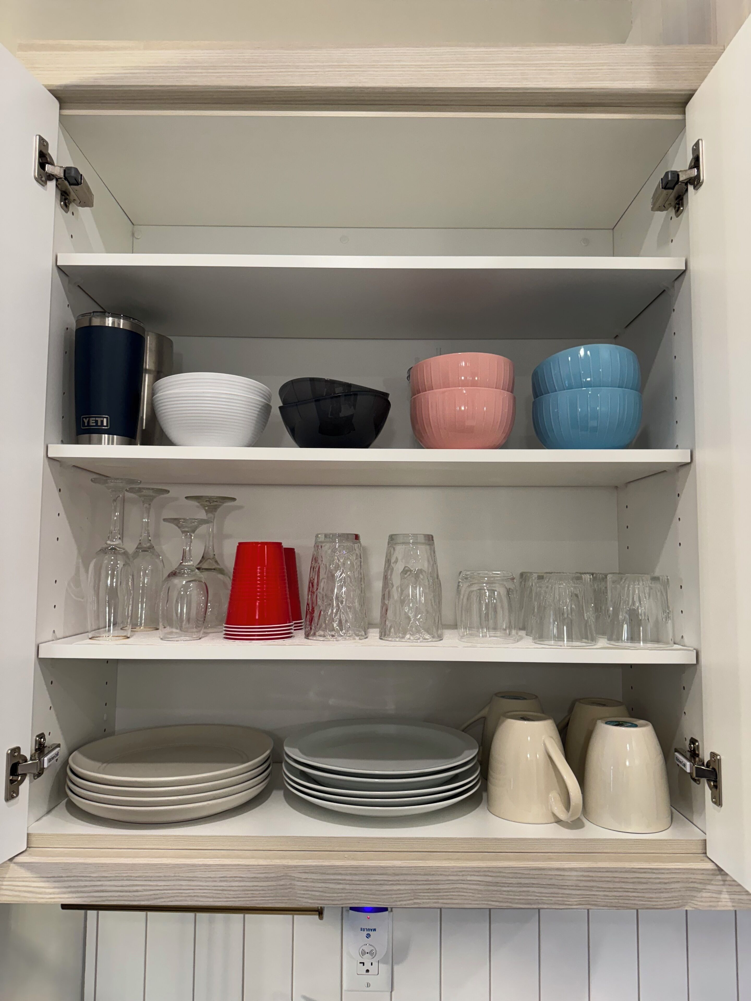 Un pensile cucina con ripiani che contengono piatti e bicchieri diversi.