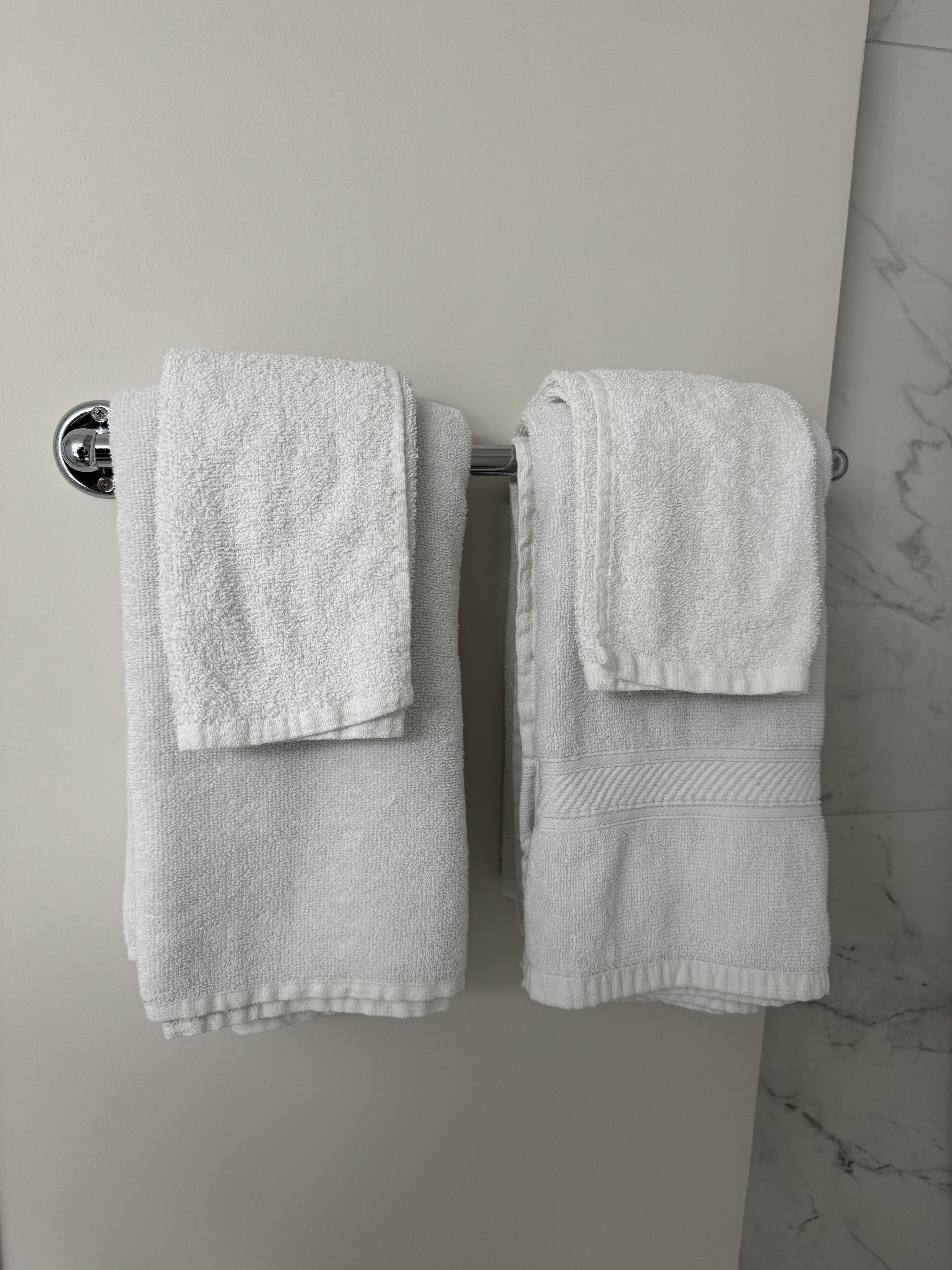 Twee witte handdoeken hangen aan een wandrek in een badkamer met een marmeren vloer.
