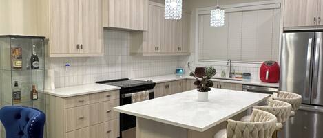 A modern kitchen with light wood cabinets, a central island, bar stools, and stainless steel appliances.