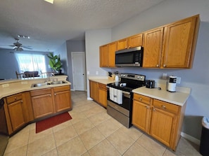 A kitchen with wooden cabinets, a microwave, a stove, and a sink. - 5BR Ocean-Themed Villa w/Private Pool Near Disney (Davenport)