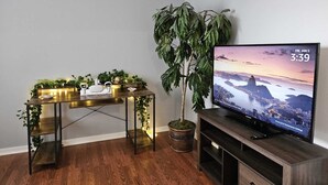 Ein Wohnzimmer mit einer Holz-Unterhaltungsanlage, einem Fernseher, der eine städtische Sonnenuntergangslandschaft zeigt, und einer großen Topfpflanze.