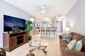 A living room with a television, a glass coffee table, a brown sofa, and a ceiling fan.