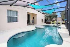A swimming pool with a covered patio area, a chair, and a table.