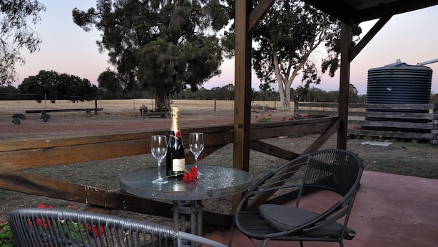 An outdoor seating area with a table set for two, featuring a bottle of wine and glasses. - Wilga Farm Stay (Wilga)