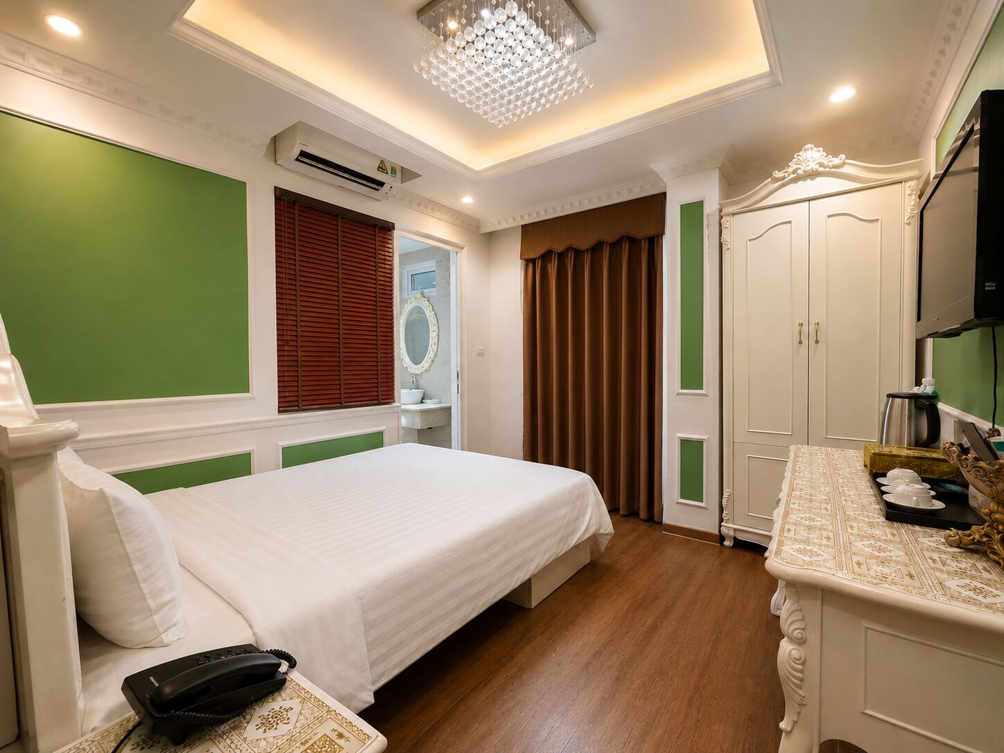 A hotel room with a bed, a vanity with a mirror, a dresser, and a chandelier.