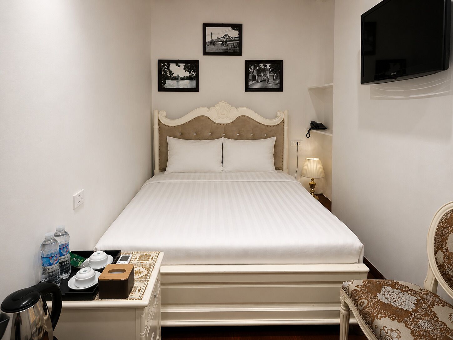 A hotel room with a bed, bedside table, chair, and wall-mounted TV.