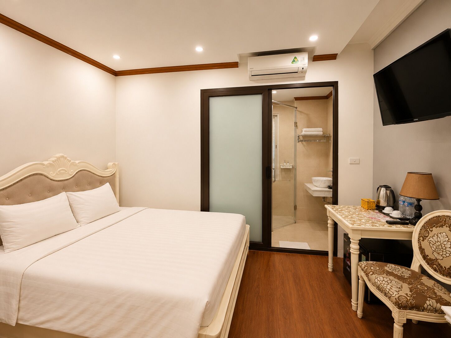 A hotel room with a bed, a desk with a chair, a television, and an air conditioning unit.