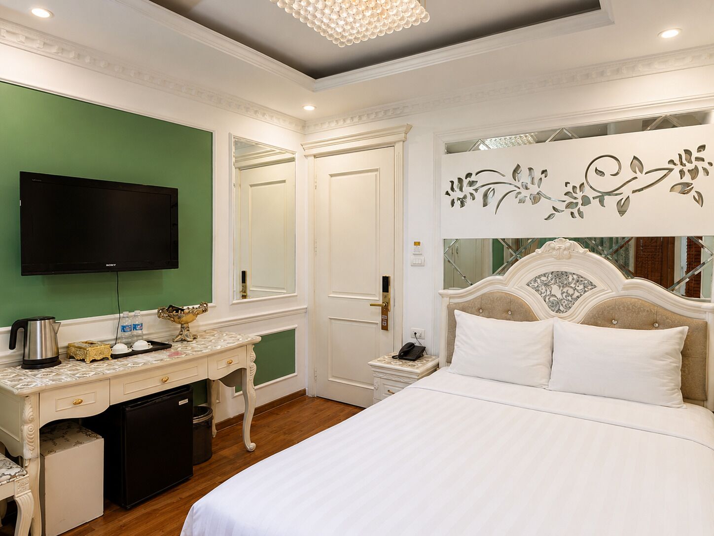 A hotel room with a bed, a desk with a television, a mirror, and a decorative wall piece.