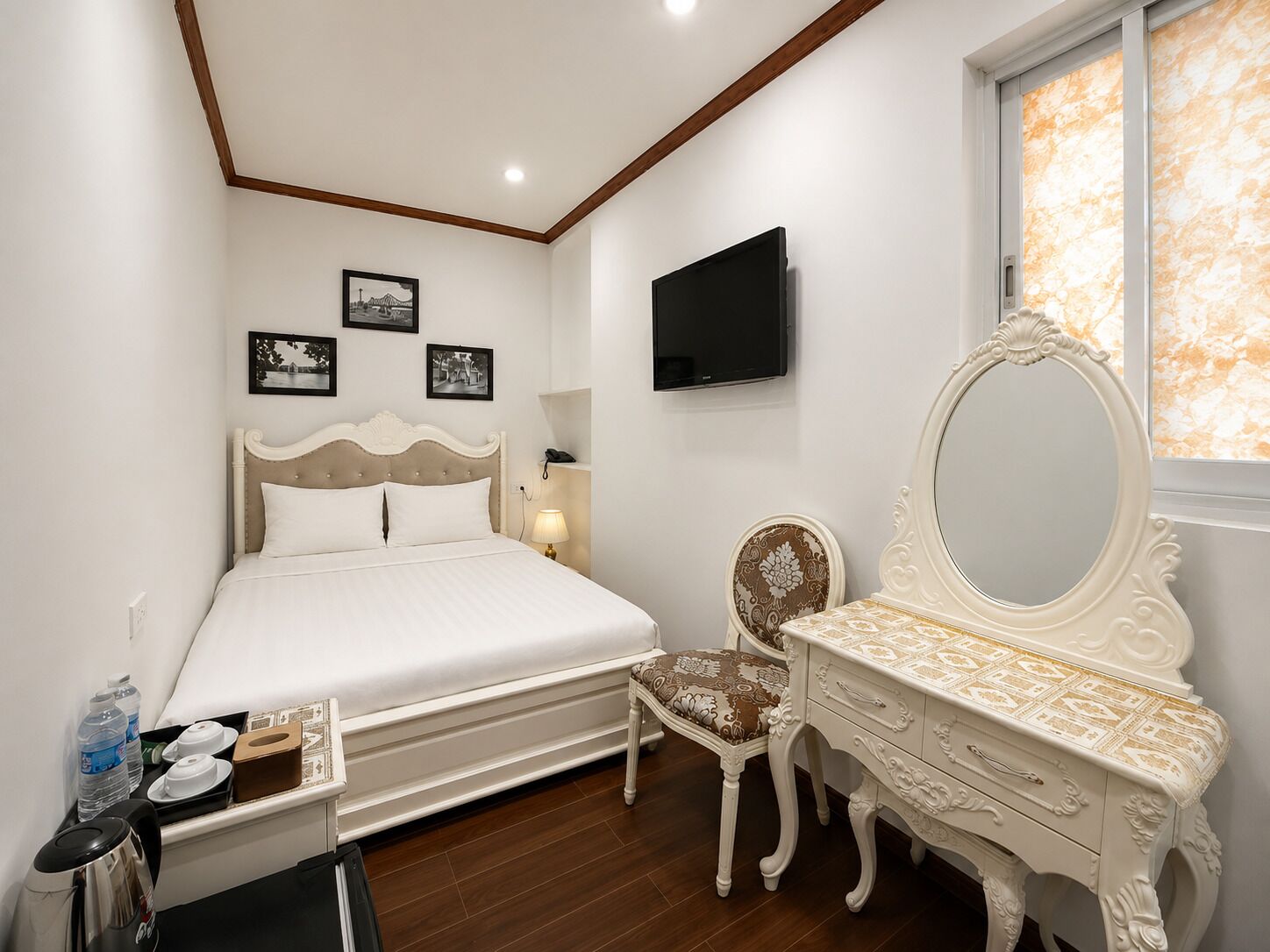 Een slaapkamer met een bed, een dressoir, een stoel, een televisie en foto's in lijsten aan de muur.