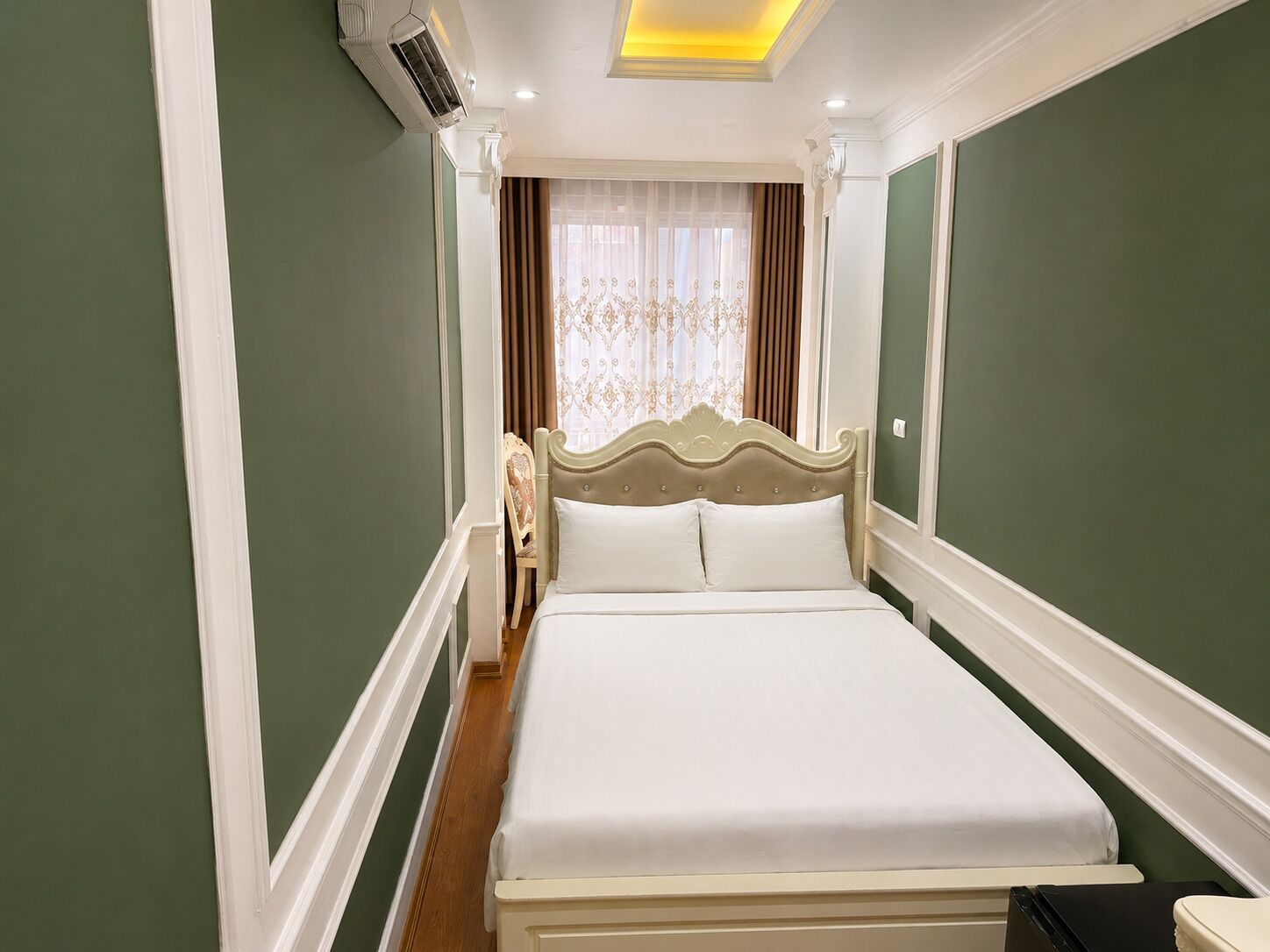 Una camera d'albergo con un letto, una sedia, un condizionatore d'aria e una finestra con tende.