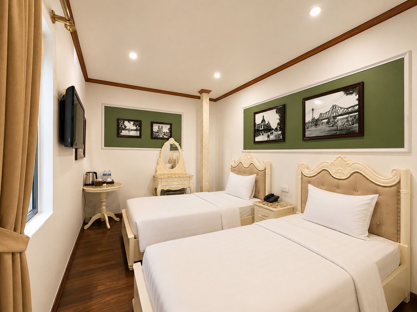 A hotel room with two beds, a vanity, a small table with a kettle, and framed pictures on the wall.