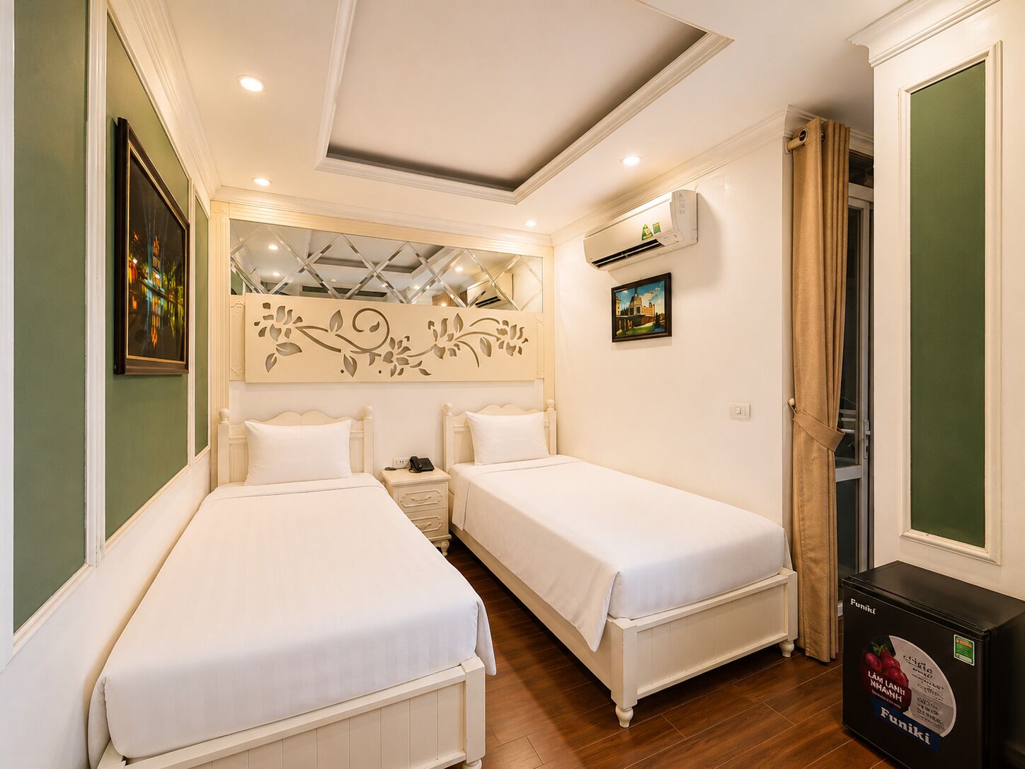 A hotel room with two single beds, a decorative ceiling, an air conditioning unit, and a small cabinet.