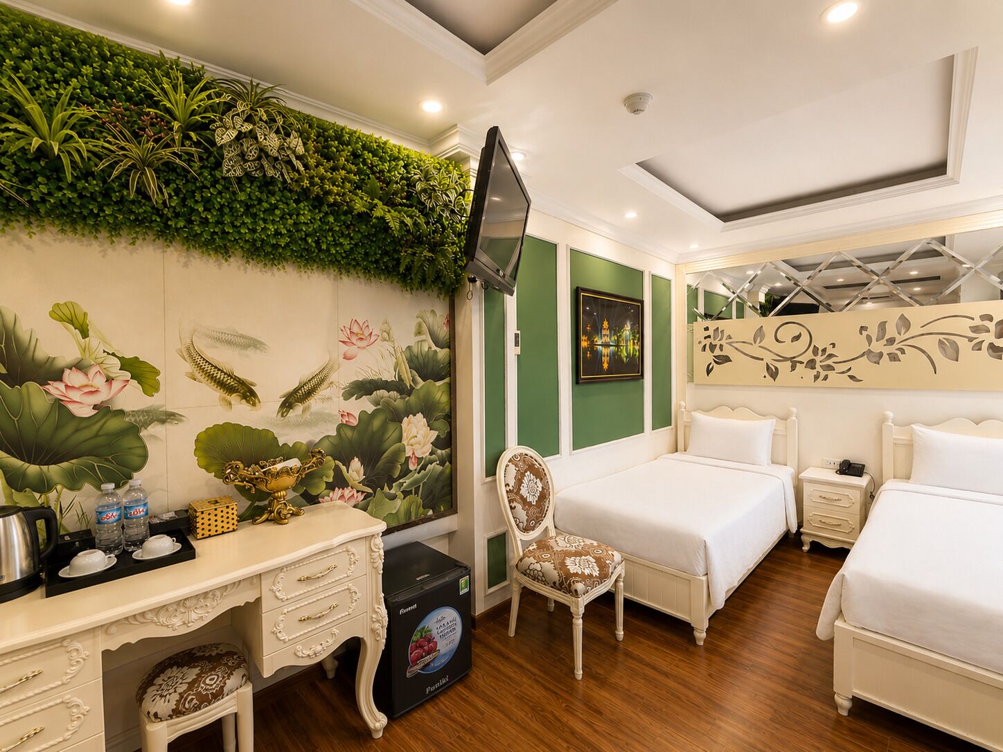 Habitación de hotel con un mural verde en la pared, una cama, un escritorio con cajones, una silla, un televisor y una mesita de noche con un teléfono.