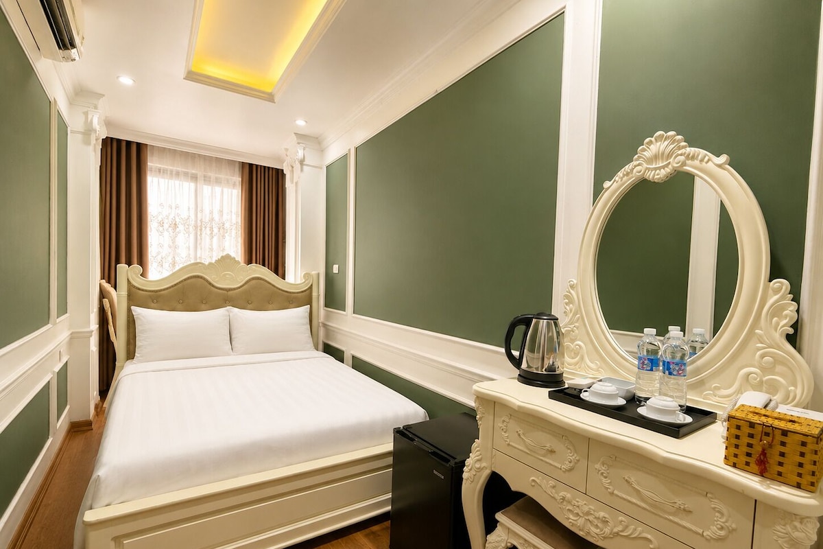 A hotel room with a large bed, a dresser, a mirror, and a small table with a kettle and cups.