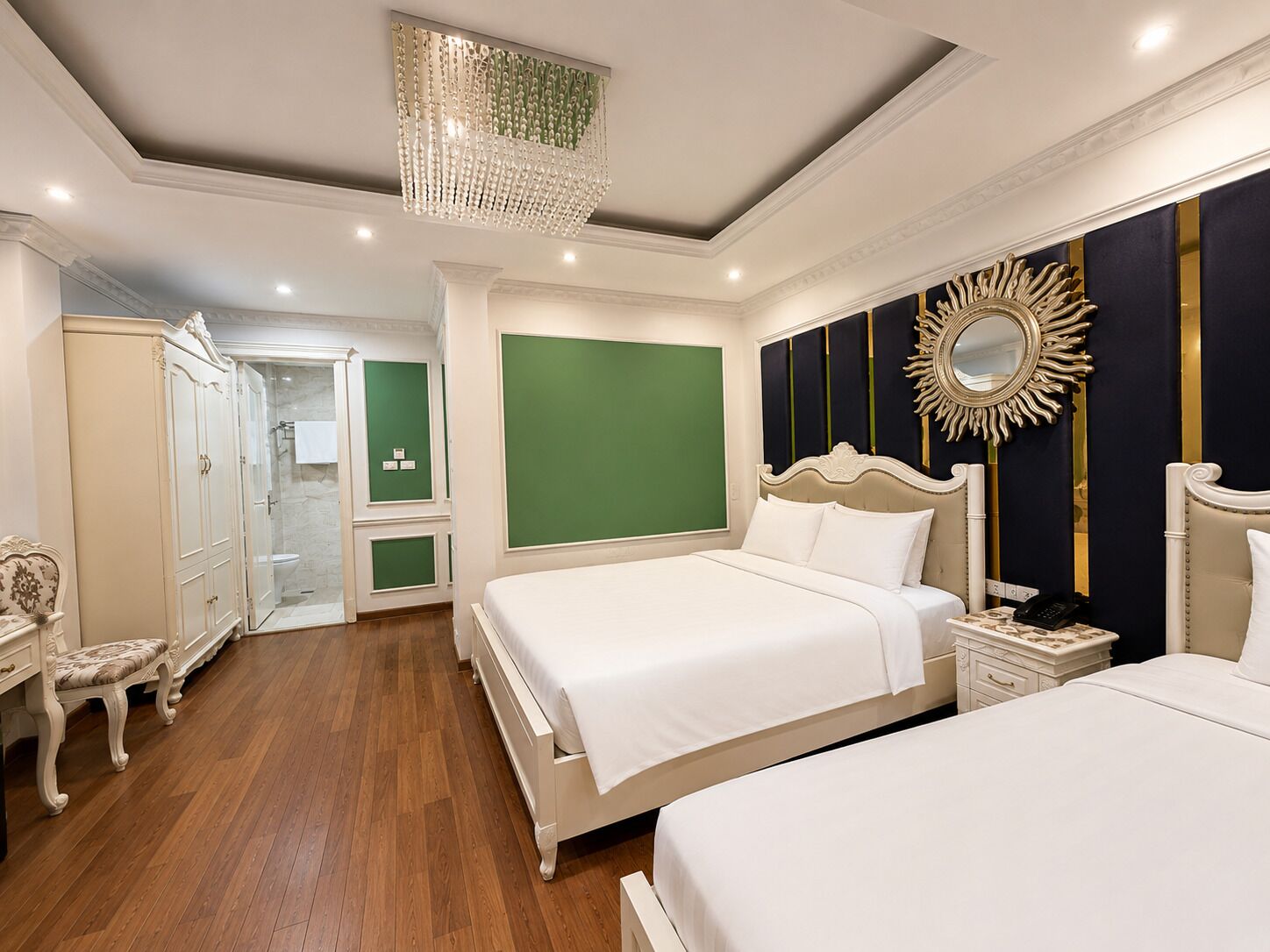 A hotel room with a large bed, a smaller bed, a vanity with a mirror, a chandelier, and a green accent wall.