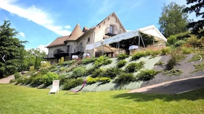 A hillside house with a steep roof, a balcony, and a garden with a chair. - Charming 'Le Gite De La Tour' with Private Terrace, Garden, and Wi-Fi (Bressieux)