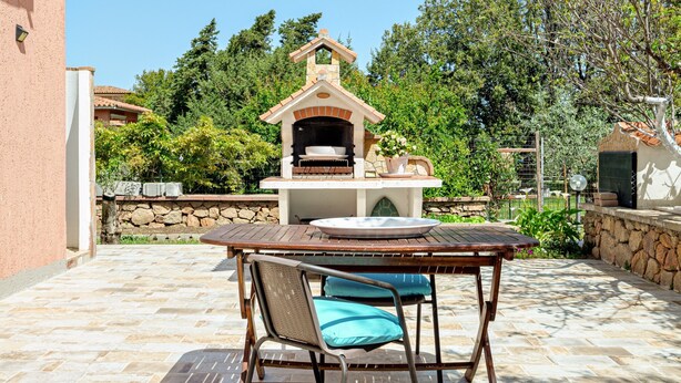 Un patio al aire libre con un muro de piedra, una mesa de madera y una estructura para barbacoa.