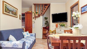 Sala de estar con sofá, mesa de comedor, sillas, televisor y una escalera que lleva a otra habitación.