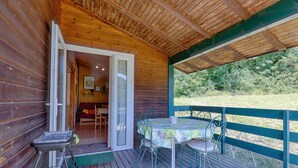 A wooden cabin with a covered deck, a table with chairs, and a sliding glass door leading to an interior room. - Chalet 'D'alpion' with Shared Pool, Private Terrace and Shared Garden (LES TOURRETTES)
