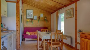 A cozy room with a wooden ceiling, a dining table with chairs, a sofa, a washing machine, and a radiator. - Chalet 'D'alpion' with Shared Pool, Private Terrace and Shared Garden (LES TOURRETTES)
