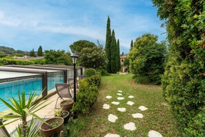 A poolside area with a clear view of the pool, a seating area with chairs, and a stone pathway leading to a garden.