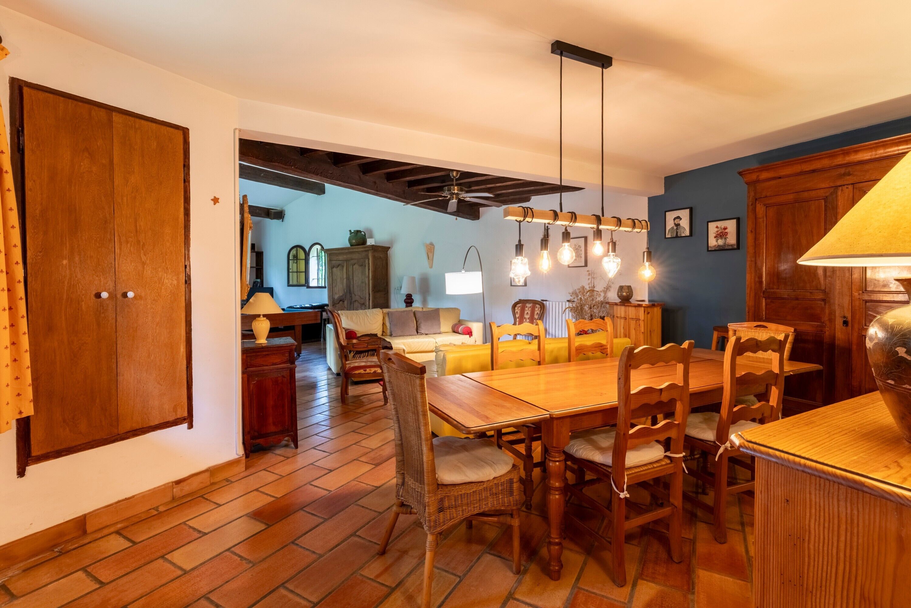 A dining area with a wooden table and chairs, a ceiling fan, and hanging light fixtures.