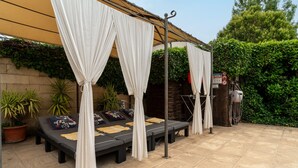 A covered outdoor seating area with cushioned benches, a pergola with white drapes, and potted plants. - Villa 'Le Colombier - Cambalala' with Mountain View, Private Pool and Wi-Fi (Barbentane)