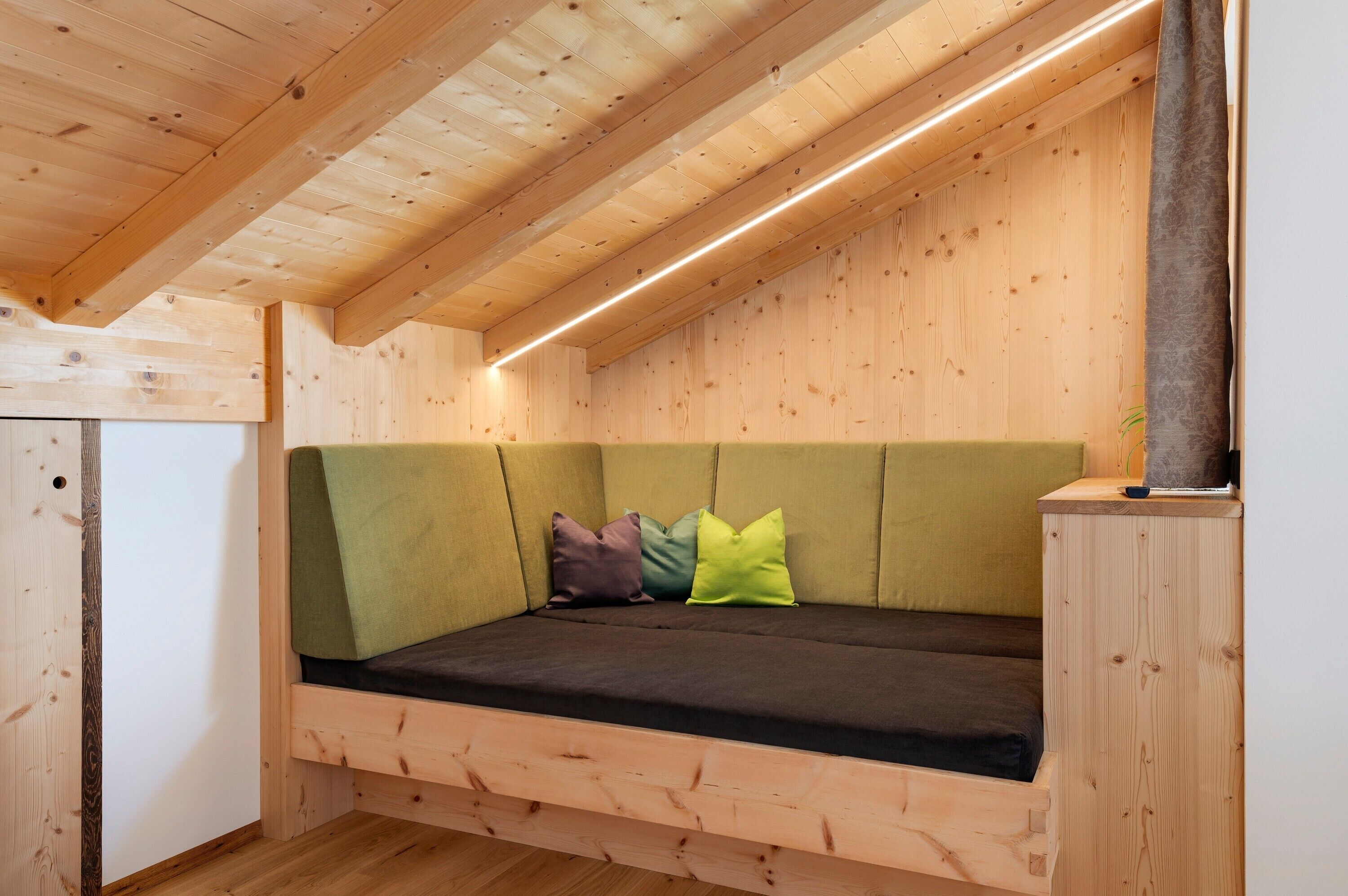 Eine Holzbalkendecke mit geneigtem Dach, ein grünes Sofa mit Kissen und ein Holzkabinett.