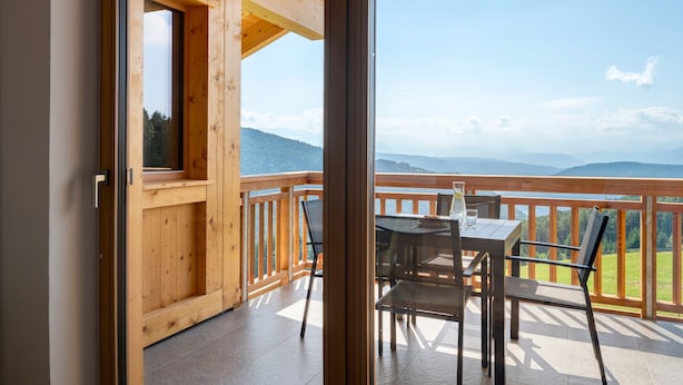 Ein Holzbalkon mit Tisch und Stühlen, der einen Blick auf eine Berglandschaft bietet.