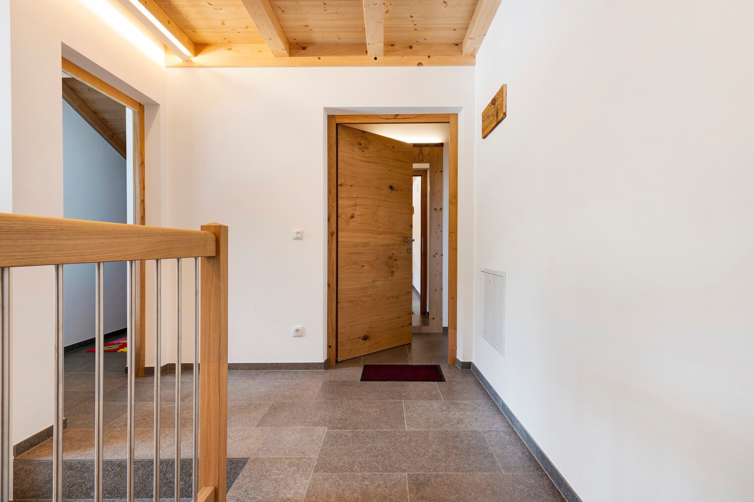 A hallway with wooden flooring, a wooden door, and a red mat at the entrance.
