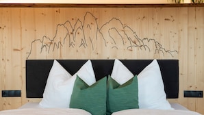 Ein Bett mit weißgrünen Kissen, einem schwarzen Kopfteil und einer Holzwand mit Bergrelief.