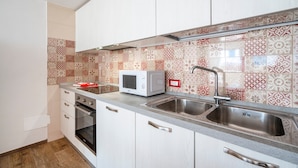 Cozinha com armários brancos, micro-ondas, pia dupla e azulejos decorativos na parede.