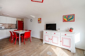 Une cuisine moderne avec des meubles blancs et un réfrigérateur rouge, un coin repas avec des chaises rouges et un meuble blanc avec des poignées rouges.