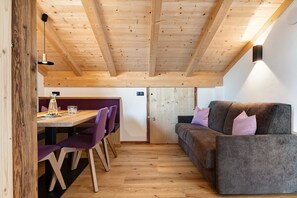 Un plafond en bois, une table à manger avec des chaises, un canapé et un luminaire fixé au mur.