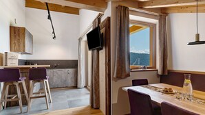 Eine moderne Küche mit Holzbalken, einem an der Wand montierten Fernseher und einem Essbereich mit Tisch und Stühlen.