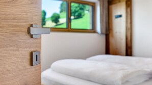 Eine Holztür mit Fenster, ein Bett mit weißer Bettwäsche und eine kleine Bedienkonsole.