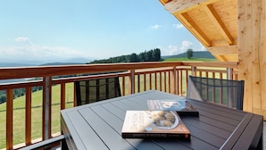 Eine Holzterrasse mit Tisch und Stühlen, ein Buch mit dem Titel 'Die Küche in Südtirol' und eine malerische Aussicht auf grüne Felder und Berge.
