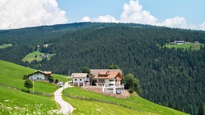 Un paisaje rural con una casa y una posada en una ladera, rodeado de bosque.