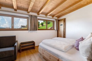 Une chambre avec un plafond en bois, un lit avec une literie blanche, un banc et une fenêtre donnant sur un paysage verdoyant.