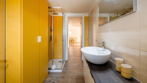 Ein Badezimmer mit einem großen weißen Waschbecken, gelben Wänden und einer Duschkabine aus Glas.