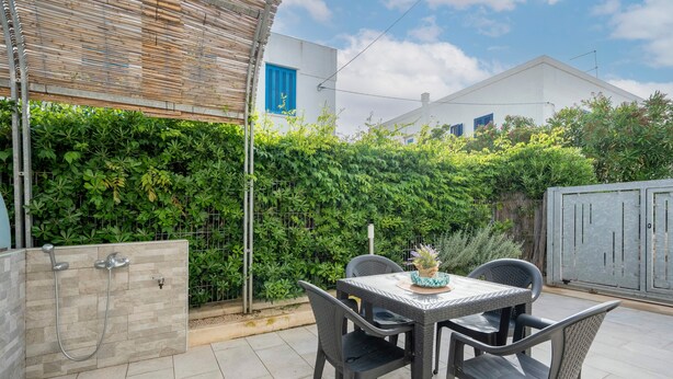Eine Terrasse mit Tisch, Stühlen, einer Duschkabine und einem Hecken.