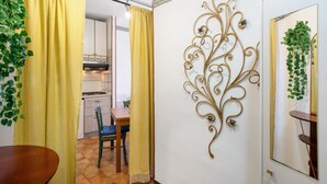 A room with a dining table, yellow curtains, a decorative wall piece, and a kitchen in the background. - Apartment 'Mare, Sole, Eucalipto' with Sea View, Private Terrace and Air Conditioning (Piani-Ciapin)