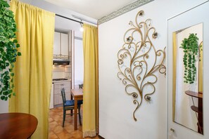 Une pièce comprenant une table à manger, des rideaux jaunes, un élément décoratif mural et une cuisine en arrière-plan.