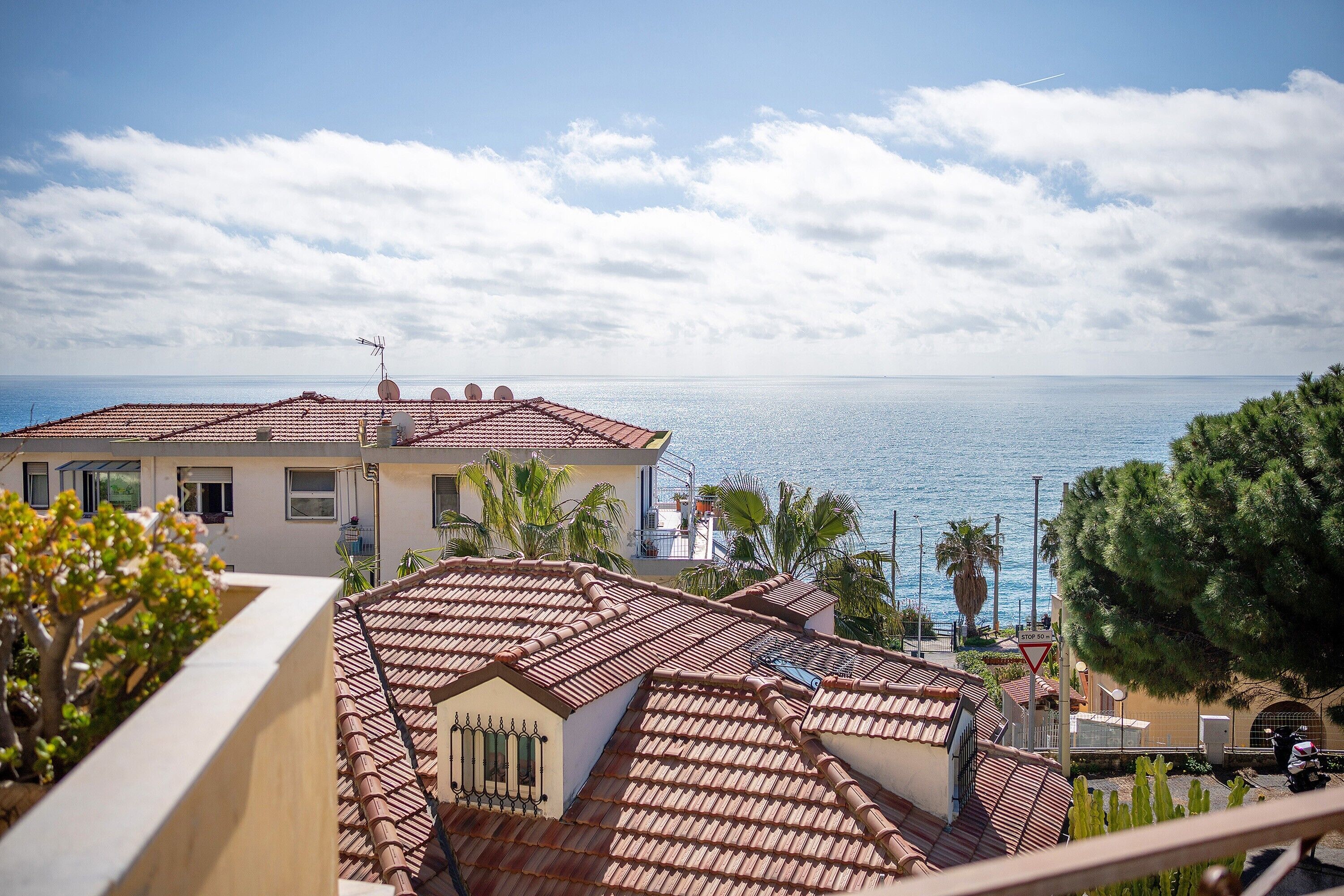 Ein Küstengebäude mit Ziegeldach, Blick auf das Meer und Palmen.