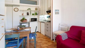 A compact kitchen with a dining table, chairs, a microwave, and a red sofa. - Apartment 'Mare, Sole, Eucalipto' with Sea View, Private Terrace and Air Conditioning (Piani-Ciapin)