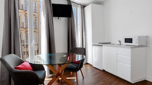Une cuisine moderne avec une table à manger en verre, deux chaises, un téléviseur à écran plat et un four à micro-ondes.